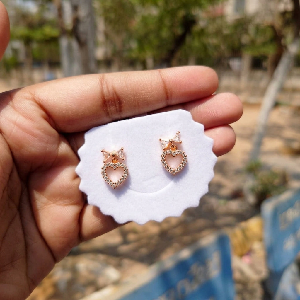 Rose gold earrings on a white card held by a hand with a blurred outdoor background