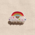 Hair clip with rainbow and cloud design on a beige fabric background