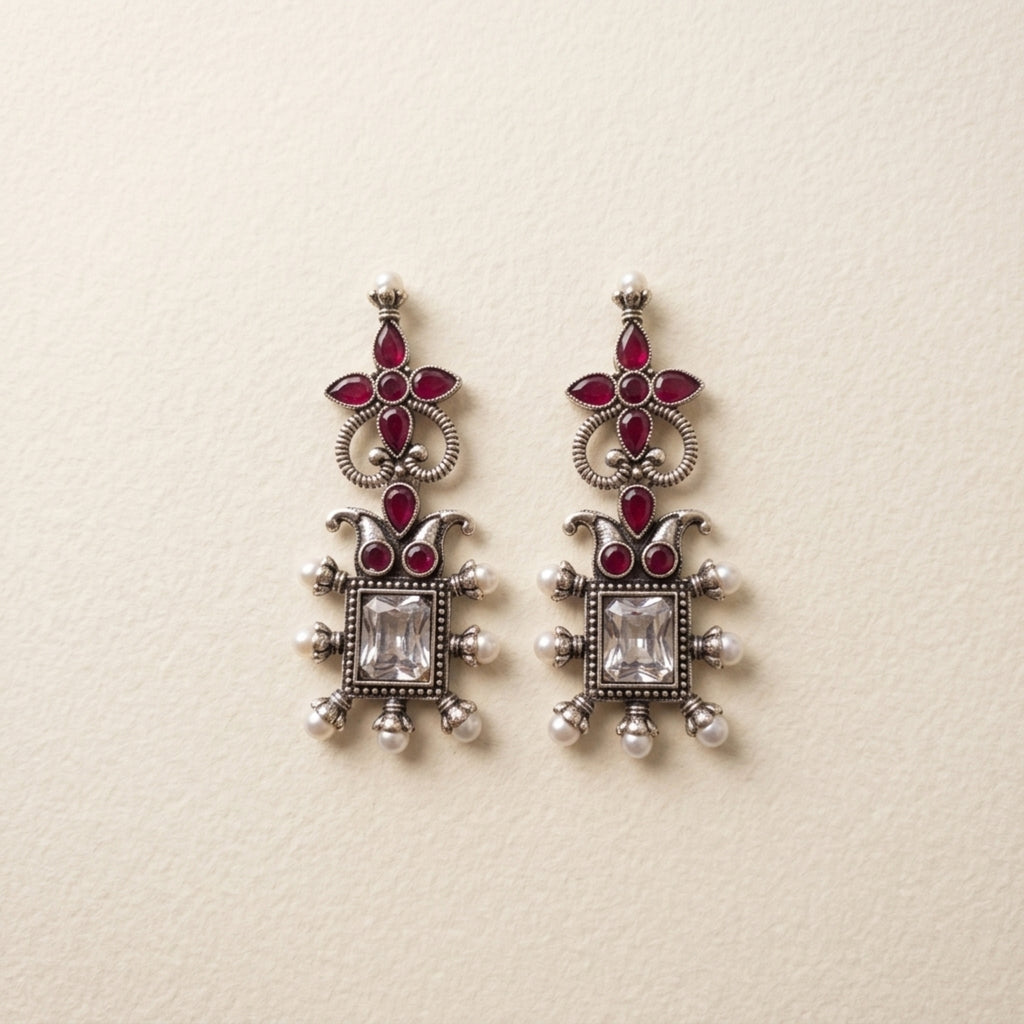 Ornate silver earrings with red gemstones on a beige background