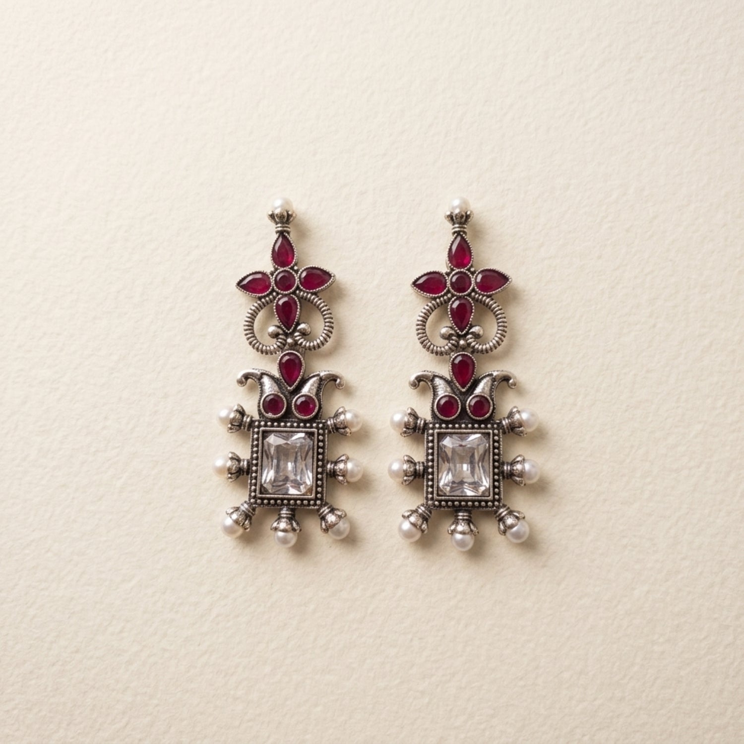 Ornate silver earrings with red gemstones on a beige background