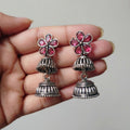 Silver earrings with pink floral tops held in a hand against a neutral background