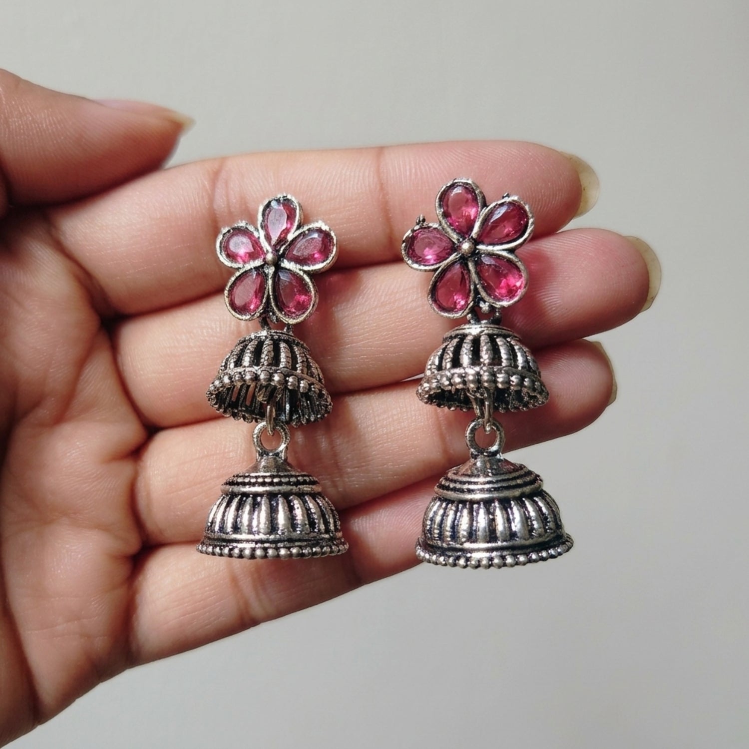 Silver earrings with pink floral tops held in a hand against a neutral background